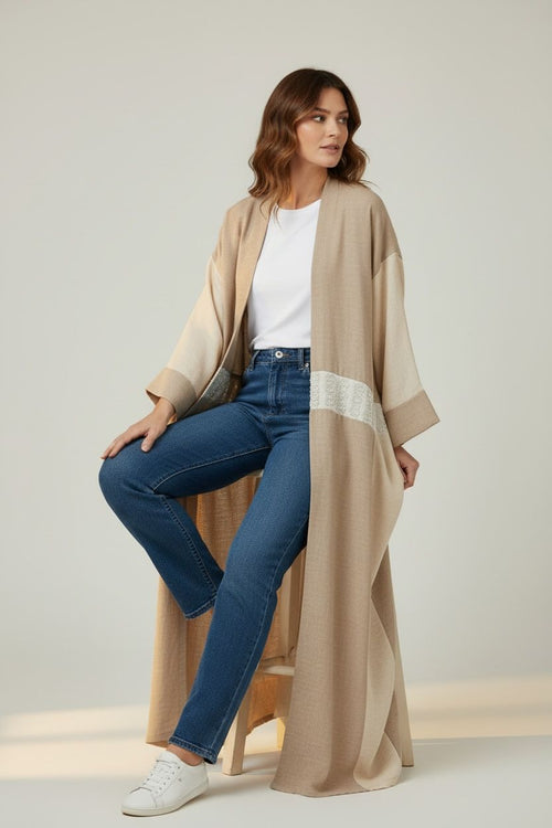Woman wearing a beige long cardigan, white shirt, blue jeans, and white sneakers on a light background